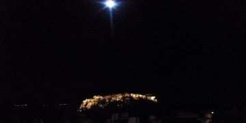 Gece aydınlatılmış Akropolis ve üzerinde yükselen dolunay